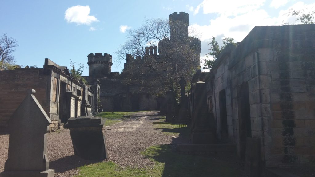 Graves and a castle at Old Calton cemetery, beneath a blue sky
