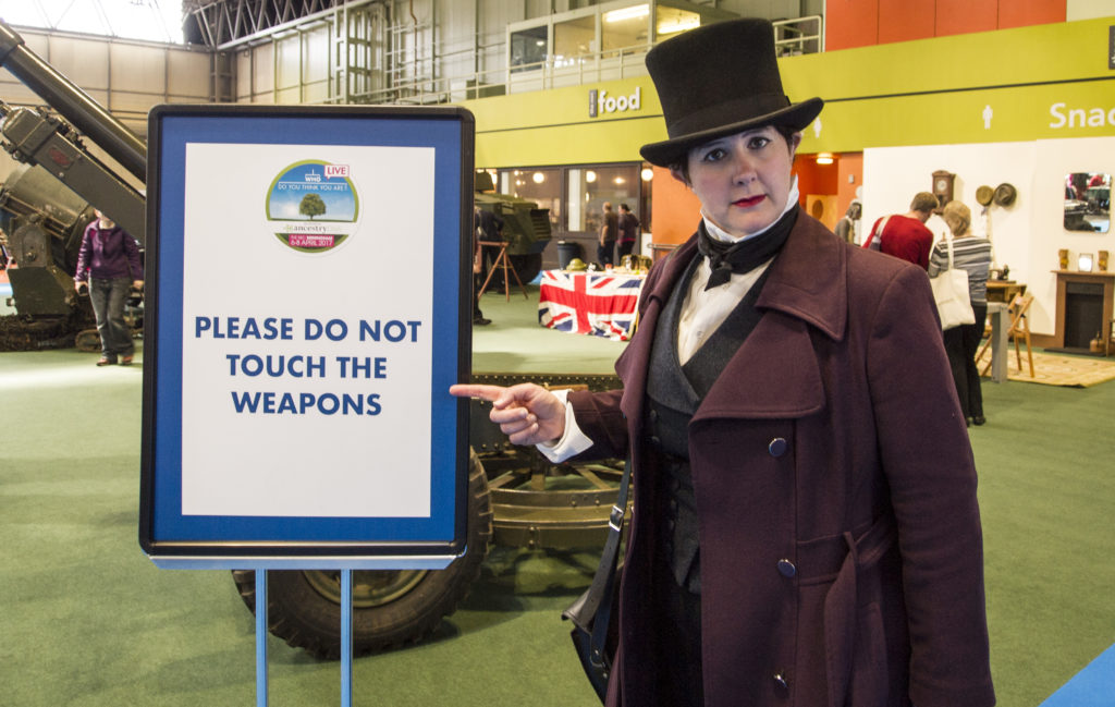Me in costume, stern of face, pointing to a sign saying "Please do not touch the weapons." In the background, you can just about see some items of WW2 military hardware.