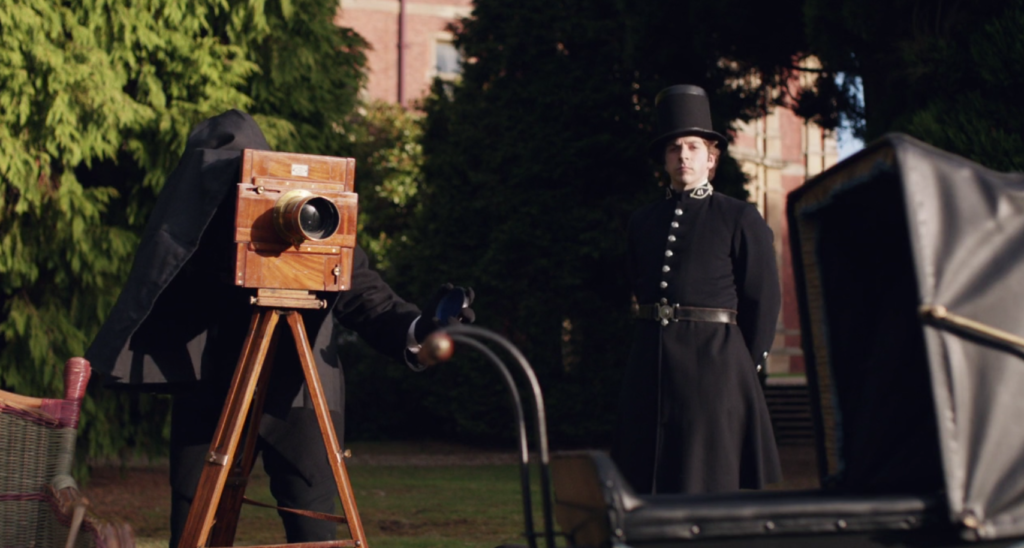 A Victorian camera is set up to take a photograph of a pram. A Victorian policeman looks on.