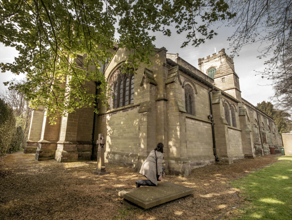 The back of the church, with what remains of the Palmer family grave, with an author in a mac carefully kneeling on it.
