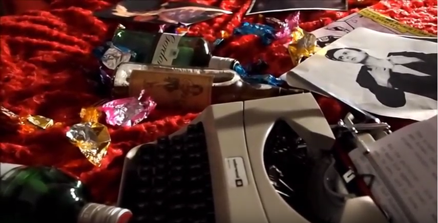 A typewriter surrounded by bottles of alcohol and sweetie wrappers.