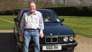 Actor Robert Hardy stands in front of a BMW car with the registration plate 666 RH