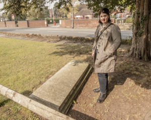 A gravestone lying on the ground in the shade of a tree, with me standing next to it.